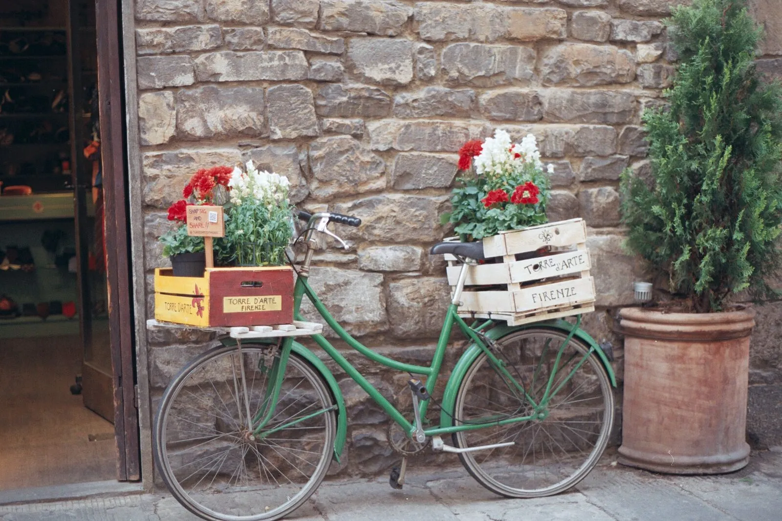 Green bicycle with flower baskets against a Tuscan stone wall