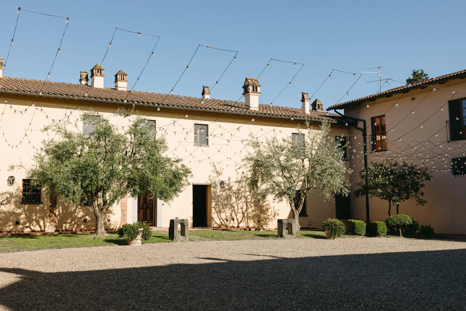 Tuscan farmhouse courtyard with olive trees, gravel and cream-coloured facade