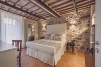 Il letto matrimoniale contro il muro in pietra viva, sotto le travi di castagno