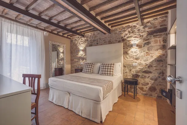 Il letto matrimoniale contro il muro in pietra viva, sotto le travi di castagno