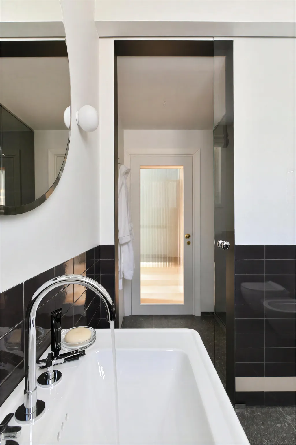 Il lavabo, lo specchio tondo e la porta a vetri rigati