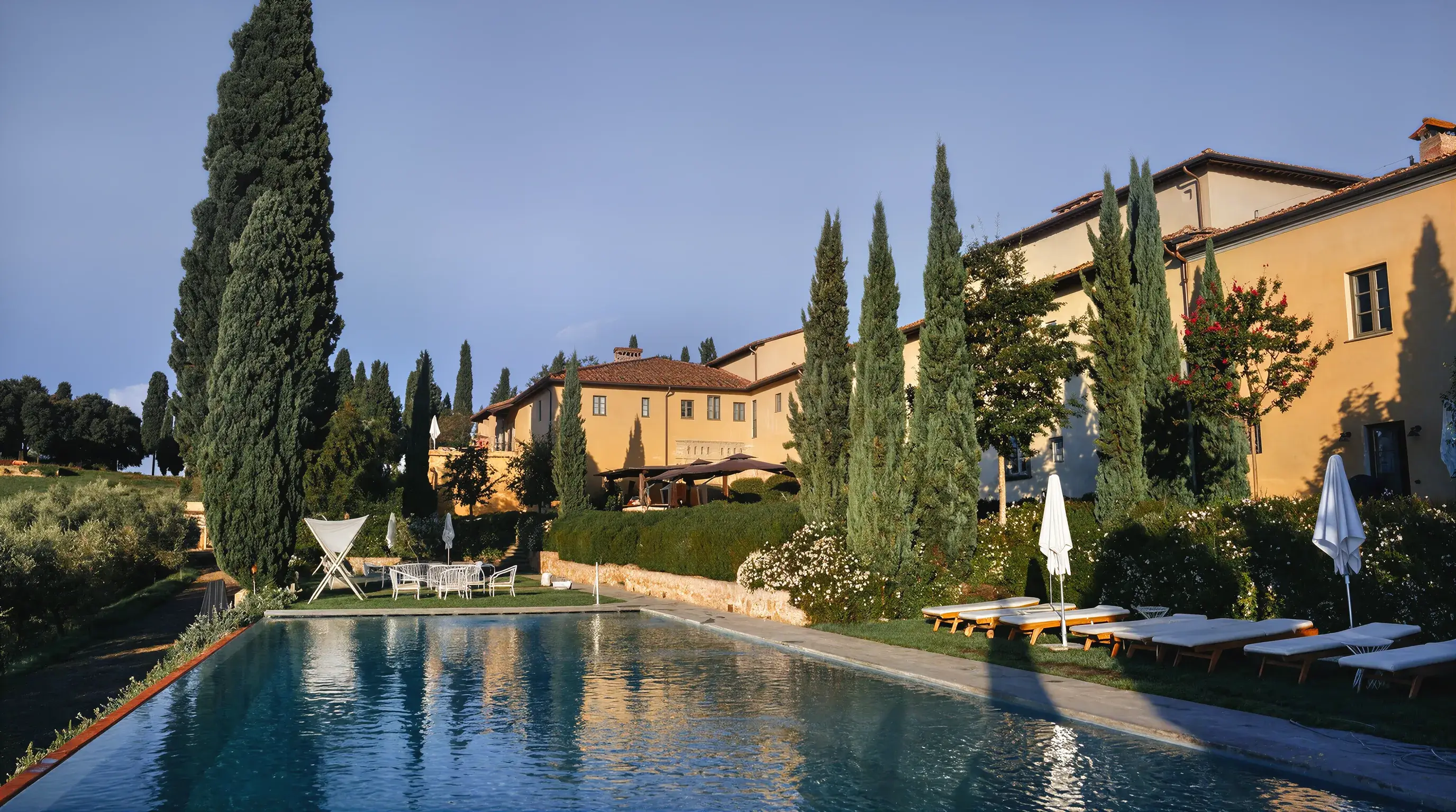 La piscina del podere al mattino, con il casolare in pietra chiara e i cipressi sullo sfondo